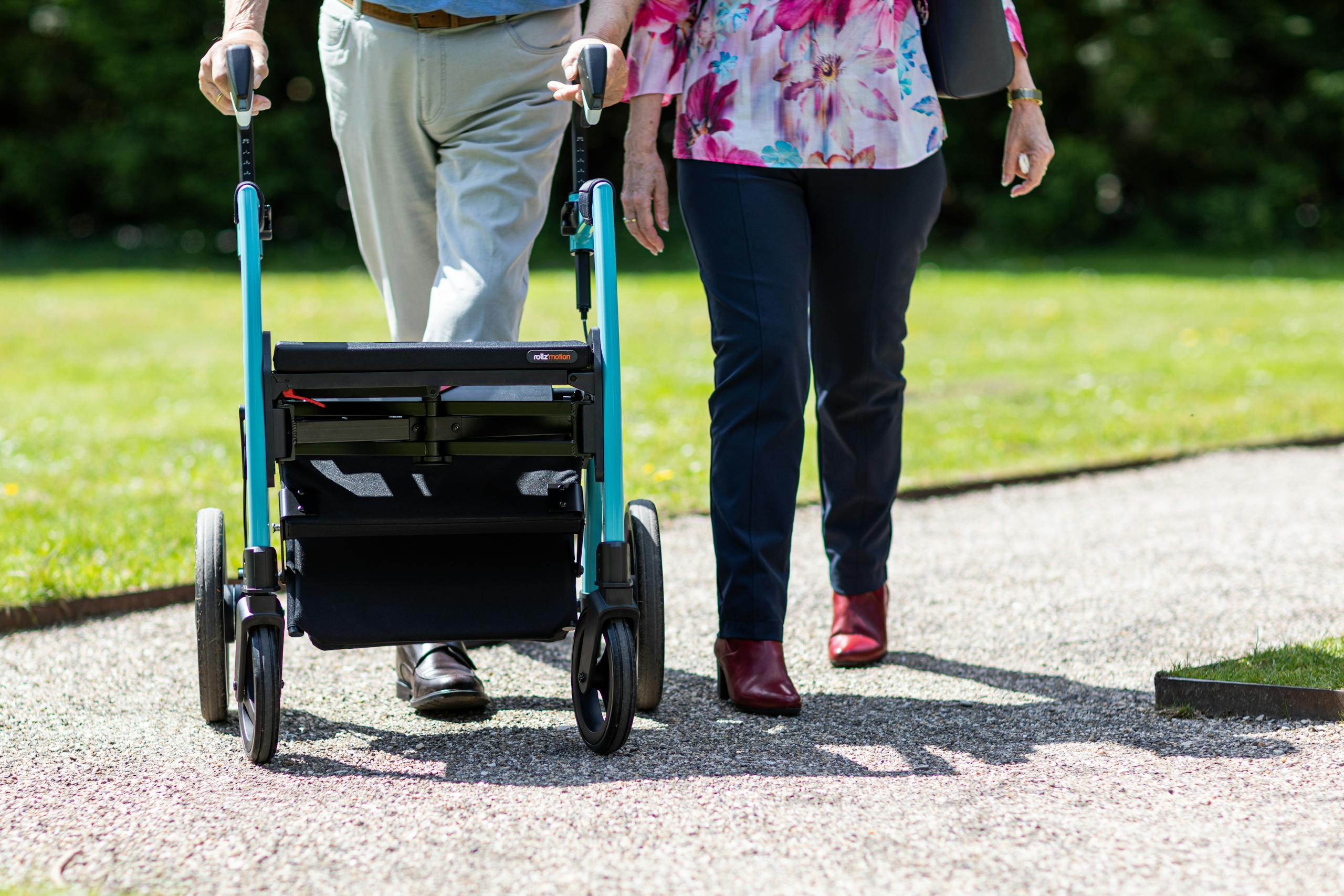 Elderly couple walking together with a walker on a sunny day in a park.